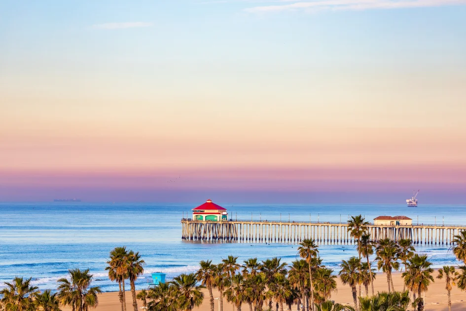 Aerial view of the Huntington Beach pier and palm trees under a pastel sky